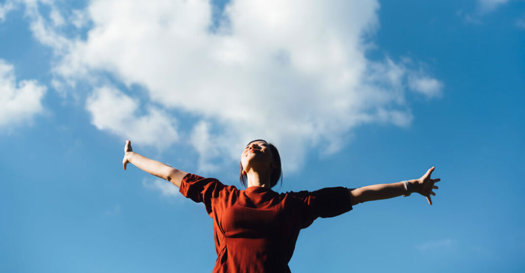 Woman outside in red shirt with her arms outstretched.