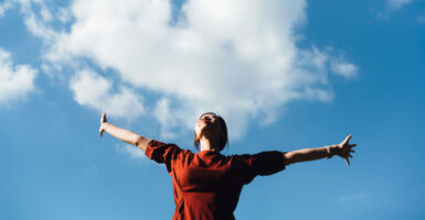 Woman outside in red shirt with her arms outstretched.