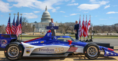 Race car driver and IndyCar Series champion Josef Newgarden speaks at the press conference for the Freedom 250 Grand Prix of Washington DC on the National Mall on March 09, 2026 in Washington, DC. In the foreground, a red, white and blue racecar.