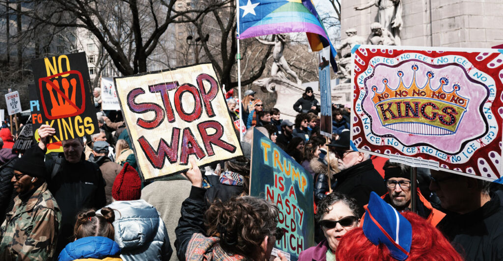 No Kings protest in New York filled with protesters and signs and a trans flag.