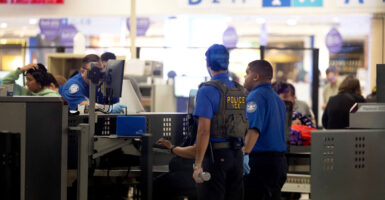 TSA agents assisted by ICE agents screen passengers at an airport.