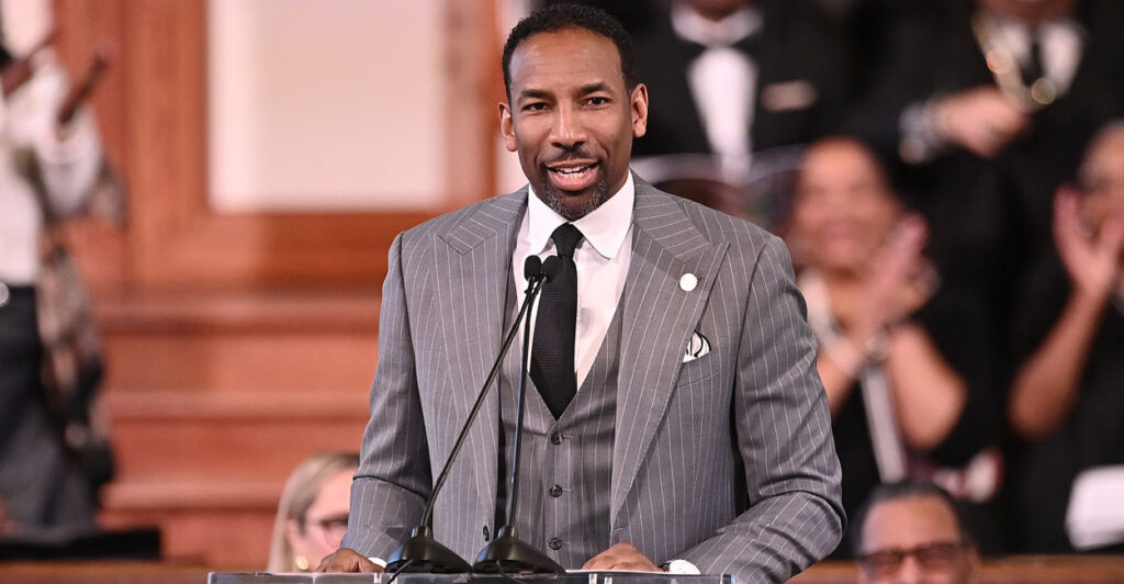 Atlanta Mayor Andre Dickens, in a grey pinstripe suit, speaks at a podium.