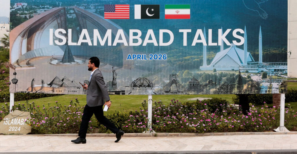 A man walks by a large sign reading "Islamabad Talks"