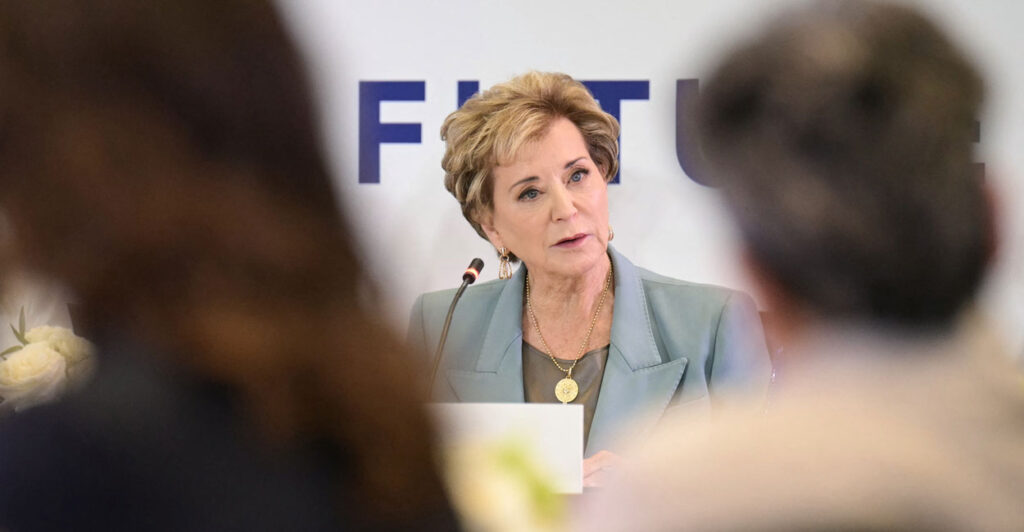 Secretary of Education Linda McMahon sits on a panel, viewed from between the heads of two women.