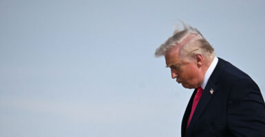 Donald Trump with his head down against a light blue sky.