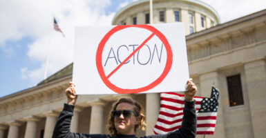 A woman stands outside of the Ohio capitol with a prohibition slash through symbol sign of "Acton"