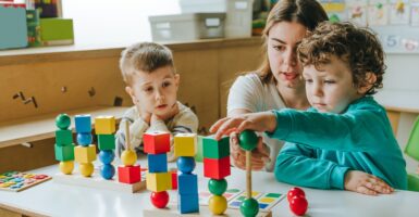 Female teacher helping little boy sort the cubes by color in a kindergarten