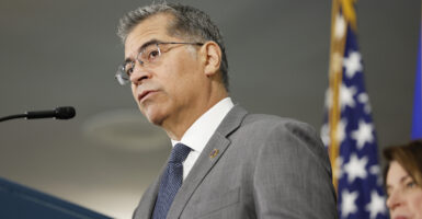 Health and Human Services Secretary Xavier Becerra stands at a podium with an American flag in the background.