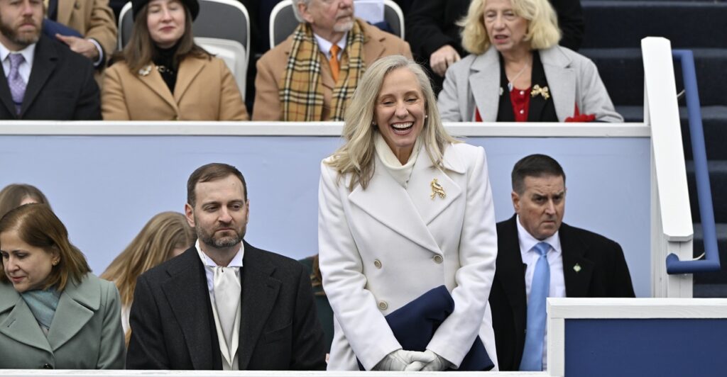 Abigail Spanberger standing and smiling in a white coat with other people seated nearby