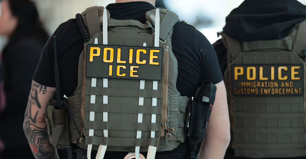 Two ICE agents have their back turned and uniform on display.