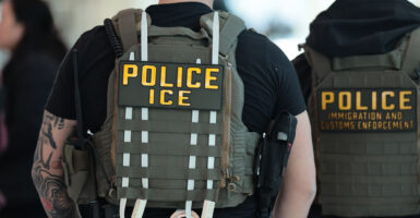 Two ICE agents have their back turned and uniform on display.