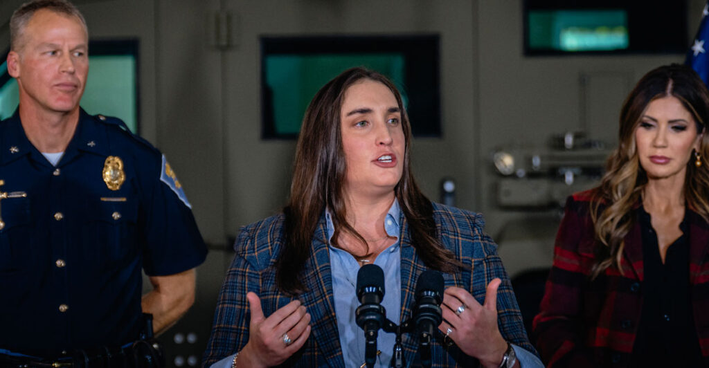 Former Immigration and Customs Enforcement Deputy Director Madison Sheahan stands in the center of a podium at a press conference.